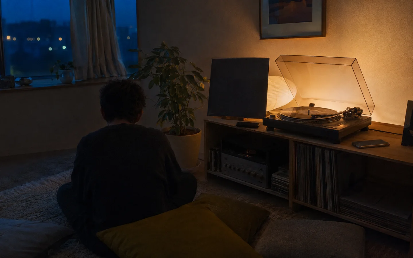 A listener sitting near a turntable in a dim room